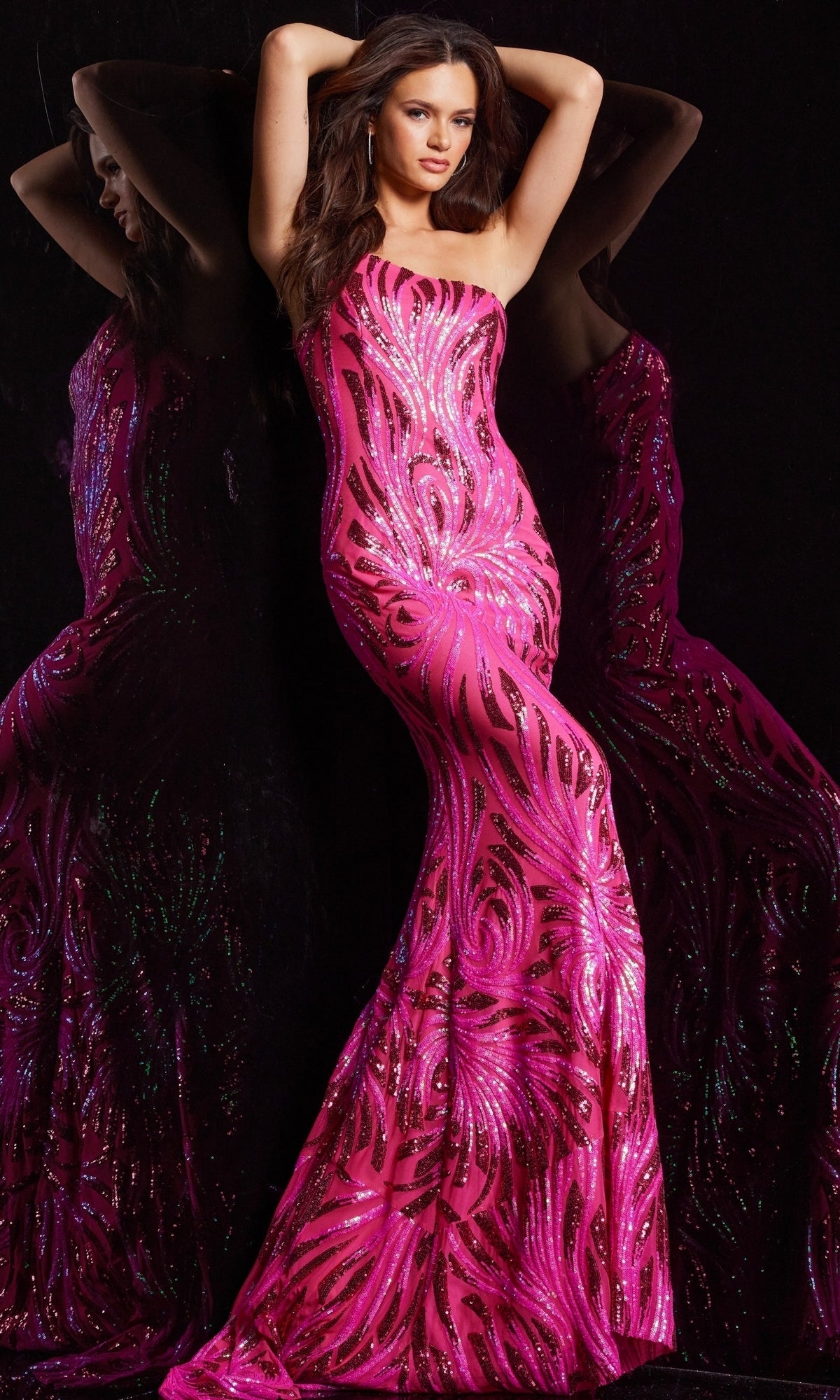 A woman models the Jovani One-Shoulder Sequin Long Prom Dress 23876, a form-fitting, floor-length fuchsia gown with swirling sequin patterns, standing beside her reflection against a black background.
